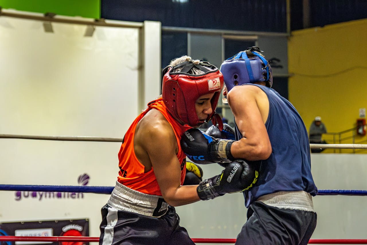 home-hero Two athletes in protective gear engage in a spirited boxing match inside a gym.